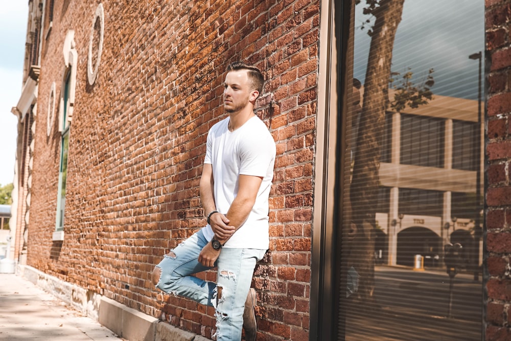 man in white crew-neck T-shirt in front of brown concrete building