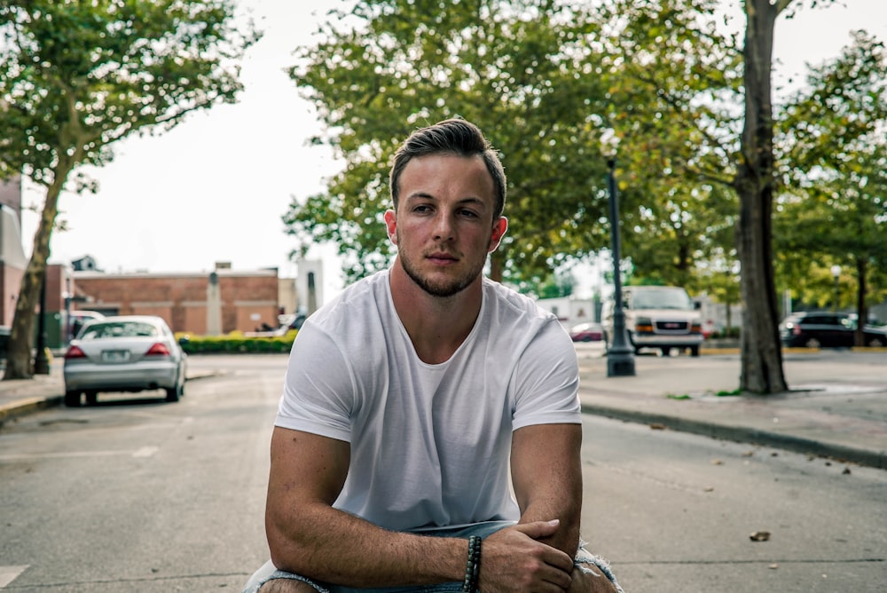 man sitting in the middle of road with two grey cars on background