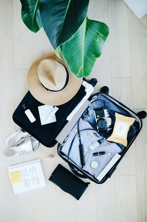 Open suitcase filled with clothes, camera, and a sun hat