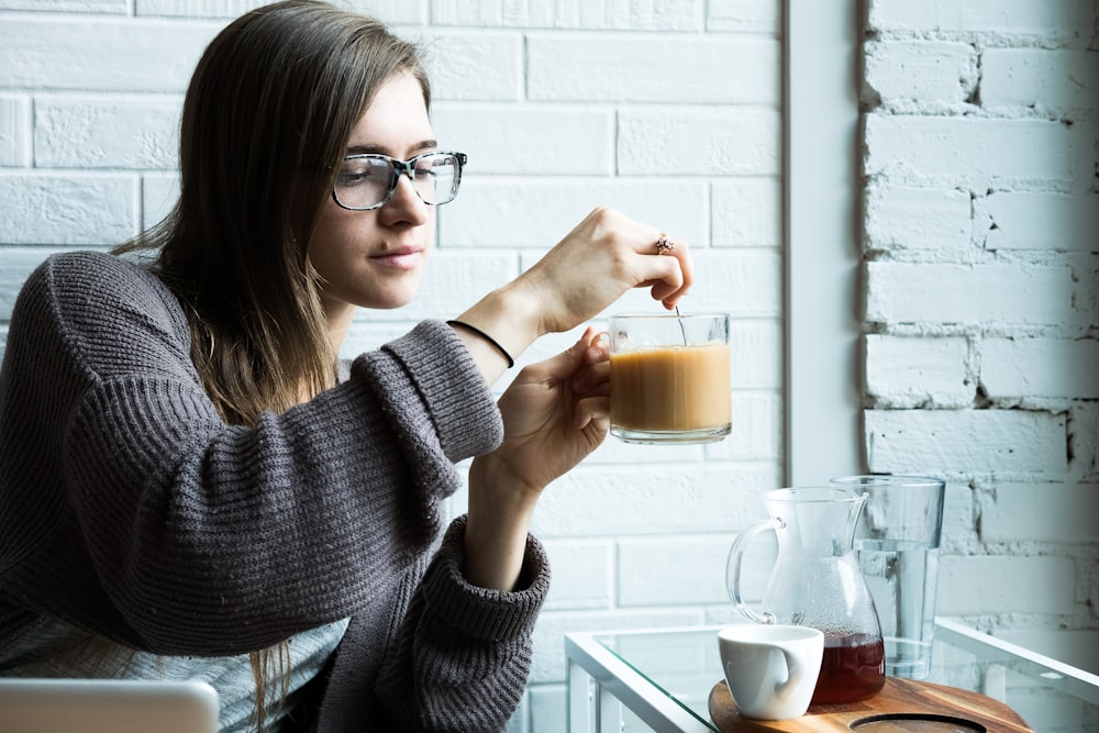 昼間にコーヒーを混ぜるグレーのニットセーターを着た女性