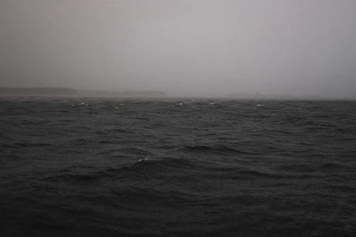 Swirling black ocean whirlpool under a cloudy twilight sky, no land in sight.