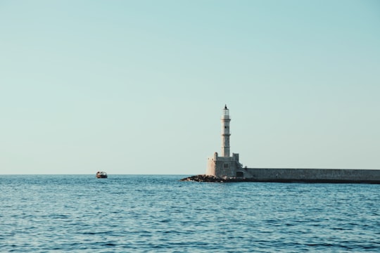 white and gray lighthouse surrounded by body of water under blue sky at daytime in Old Venetian Harbour Greece