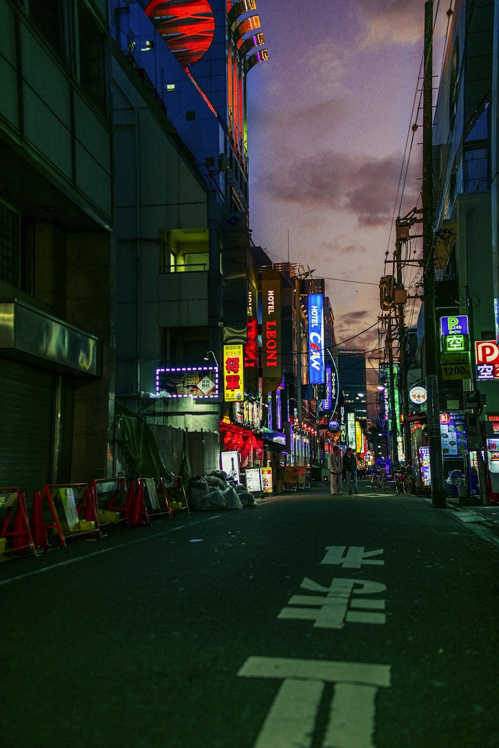 two persons standing on concrete road between buildings during nighttime