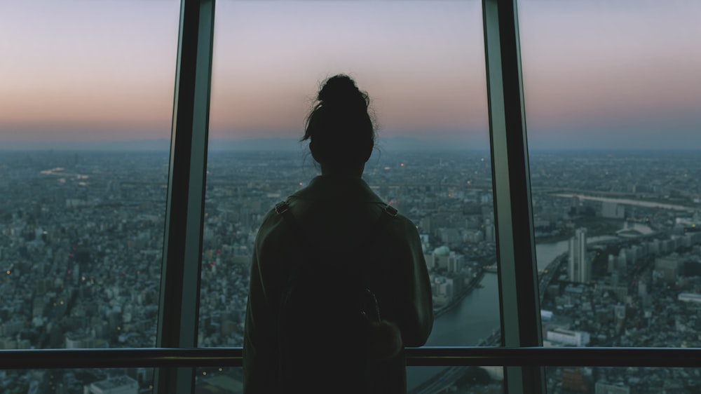 silhouette of person standing inside the building facing the glass mirror watching the city