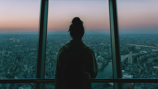 silhouette of person standing inside the building facing the glass mirror watching the city in Tokyo Skytree Japan