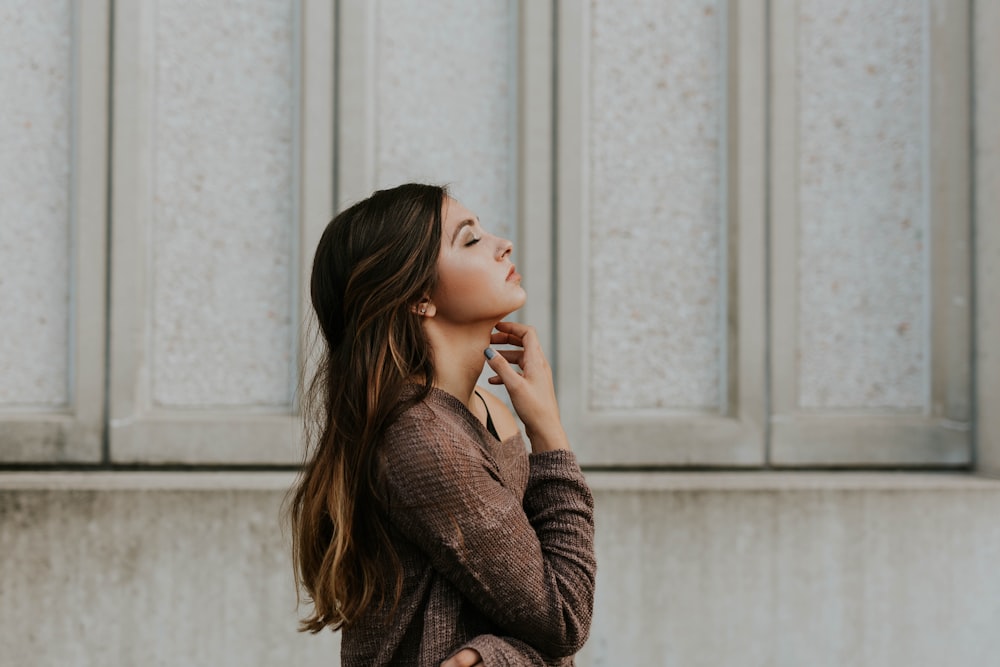 woman in brown long-sleeved top standing beside wall