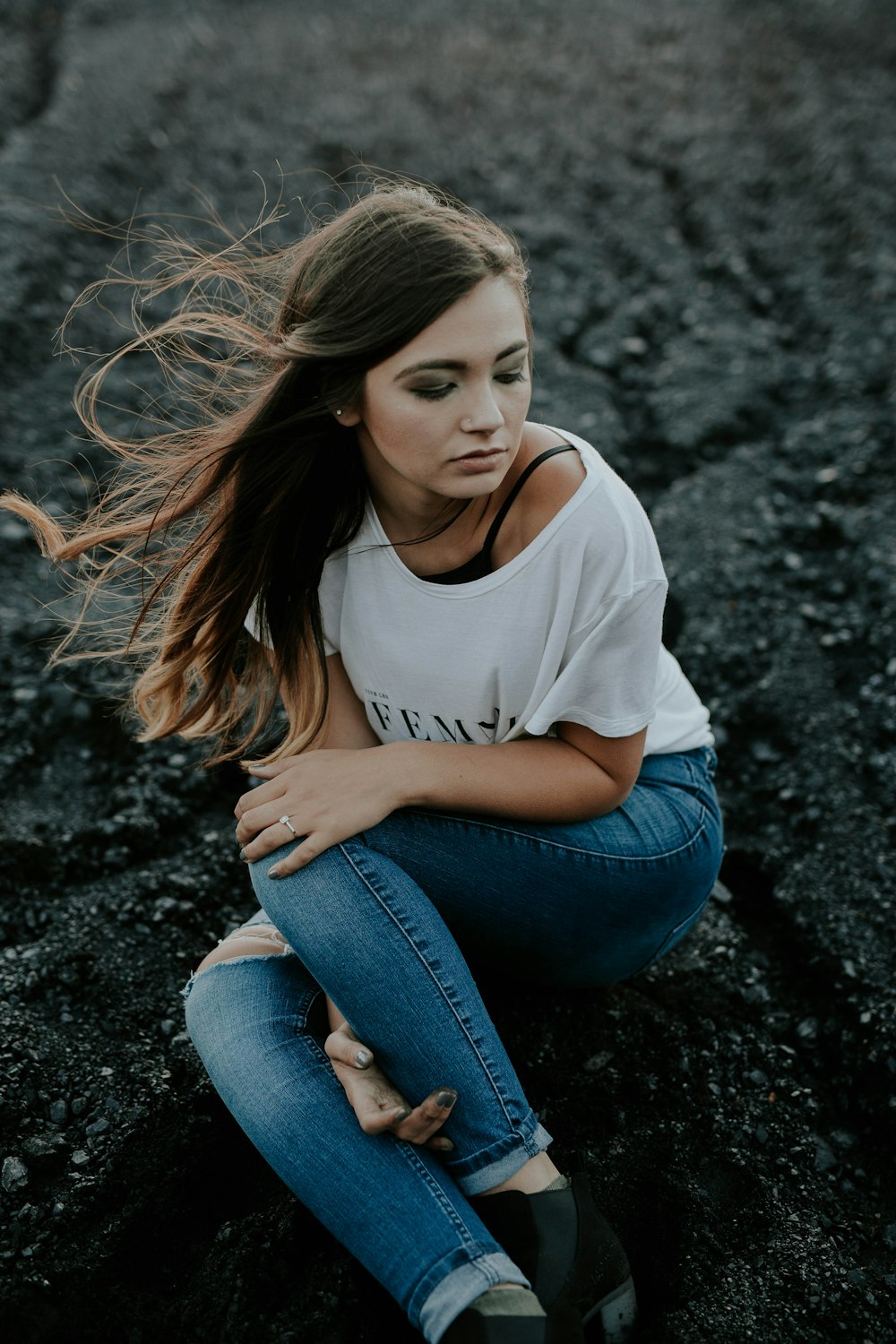 woman wearing scoop-neck shirt and distressed jeans sitting on ground while holding knee