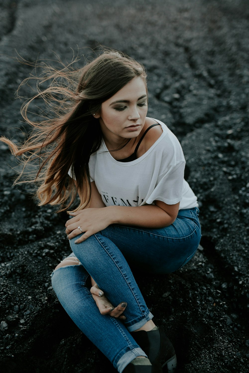 Femme portant une chemise à col rond et un jean usé assise sur le sol tout en tenant le genou