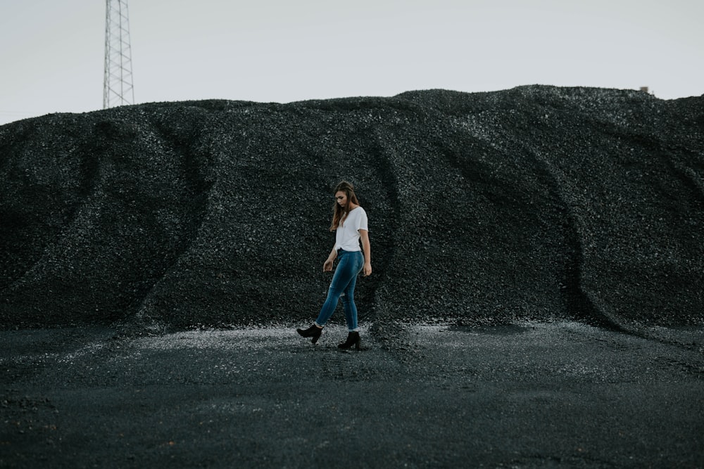 woman in white t shirt walking beside gray sand