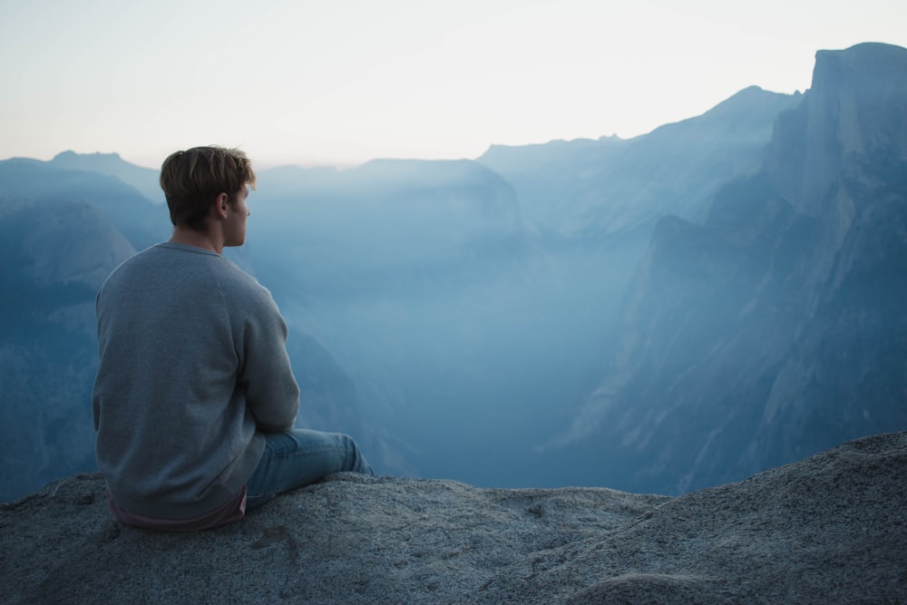 man in gray shirt sits on cliff meditating