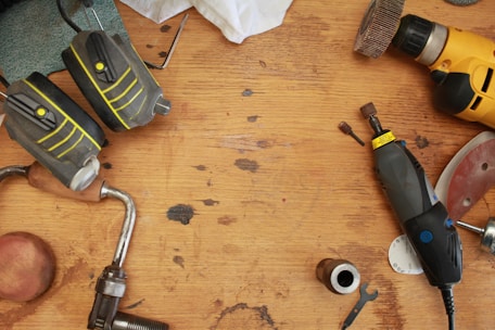 Close-up of a cordless drill resting on a wooden workbench with scattered screws