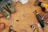 A wooden workbench scattered with various tools including a pair of ear protectors, a cordless drill, a rotary tool with attachments, a small wrench, and other metal and wood components. The tools are arranged in a disorganized manner, suggesting a busy workspace.