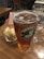 A glass of amber beer with a Brooklyn Brewery logo is placed on a wooden table, accompanied by a small bowl of potato chips and a wine glass. The setting appears to be in a casual dining environment with wooden furniture visible in the background.