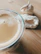 Close-up of a frothy coffee cup next to a flaky, golden pastry on a wooden table.