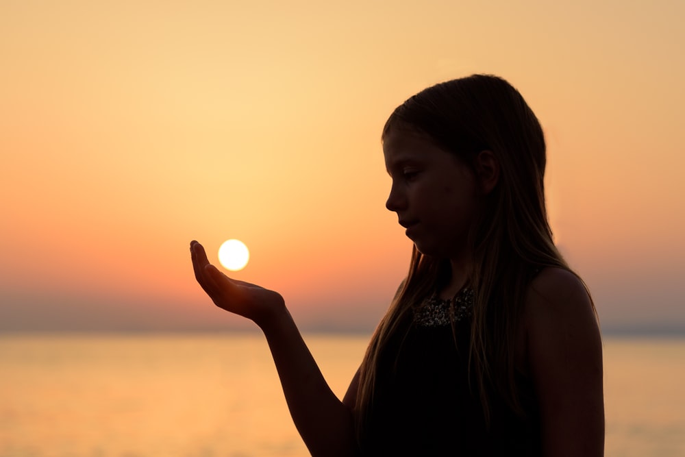 A woman in silhouette appears to hold the setting sun in her hand in Koundouros