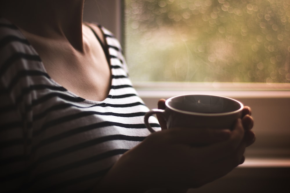 Mujer en la parte superior a rayas blancas y negras sosteniendo una taza de cerámica blanca