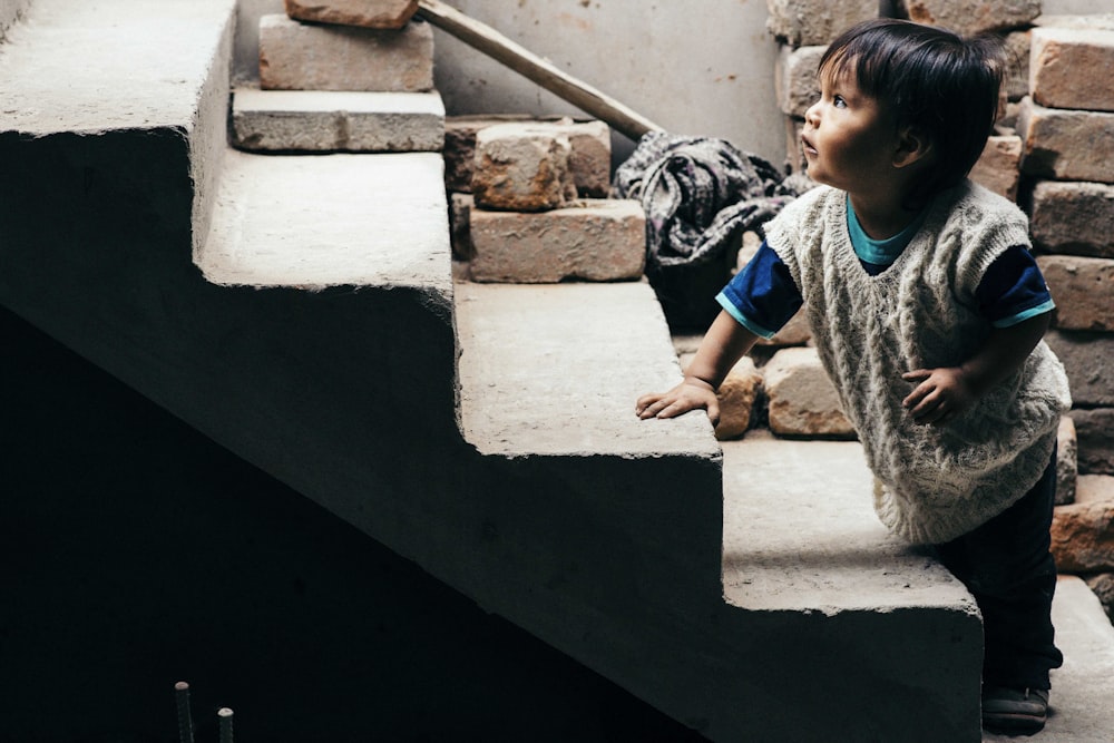 boy in gray and black crew neck t-shirt sitting on white concrete stairs