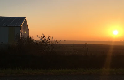 A scenic shot of a rustic farm at sunrise, highlighting rows of crops and a red barn.