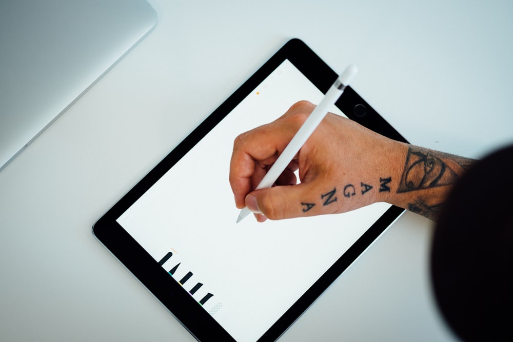 pessoa segurando caneta branca escrevendo no iPad preto