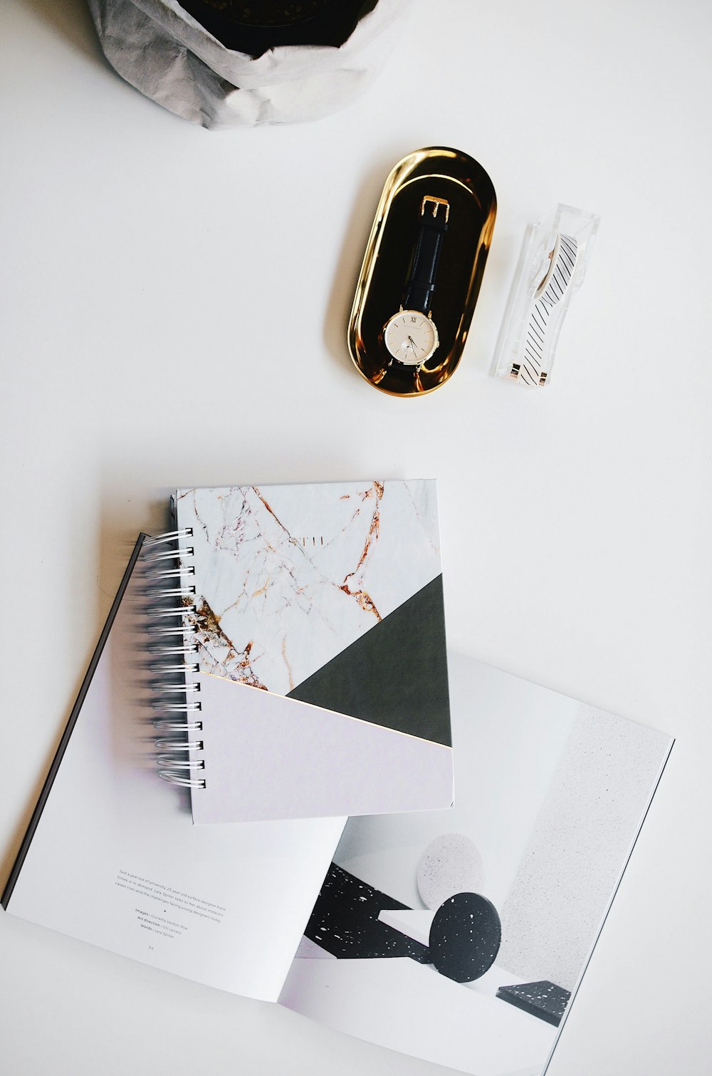 top view photography of round silver-colored analog watch with black leather strap on case near white covered notebook