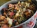 A close-up view of a bowl filled with a variety of dried herbs, fruits, and flowers. The mixture includes visible ingredients like rose petals, dried berries, and pieces of dehydrated fruit and leaves, creating a rich textural composition.
