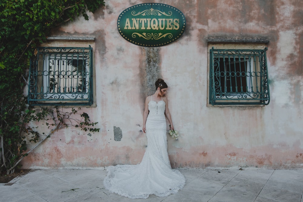woman wearing wedding gown standing near wall holding flowers