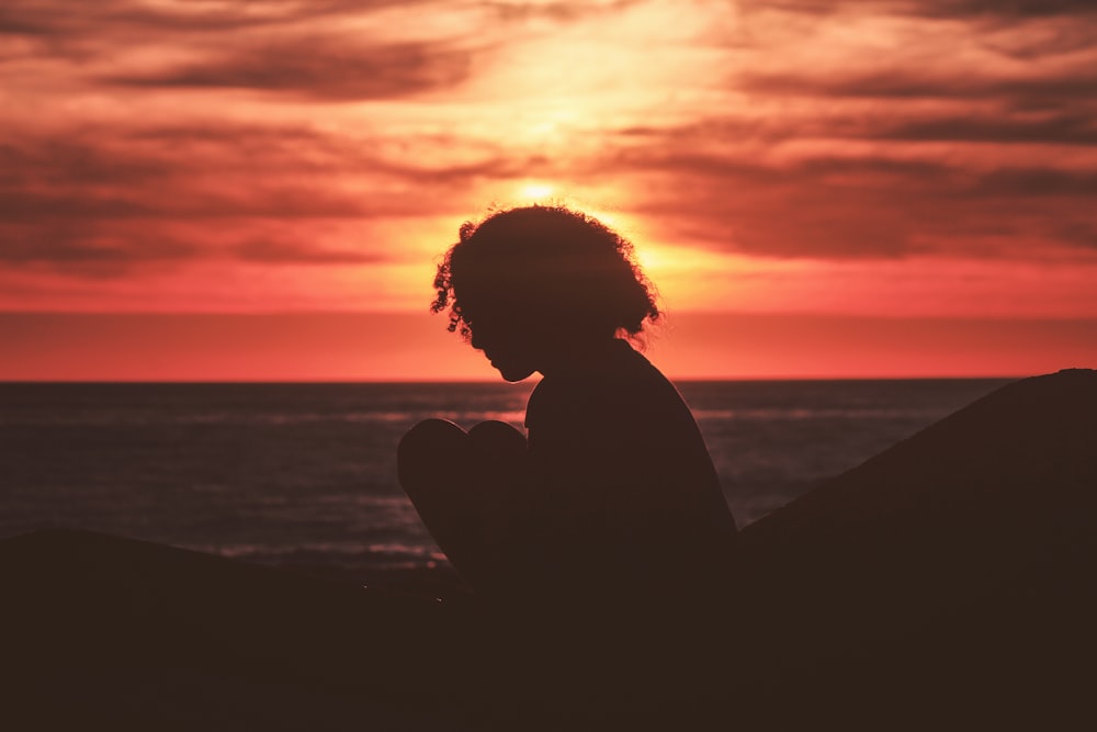 silhouette of girl sitting near sea during golden hour