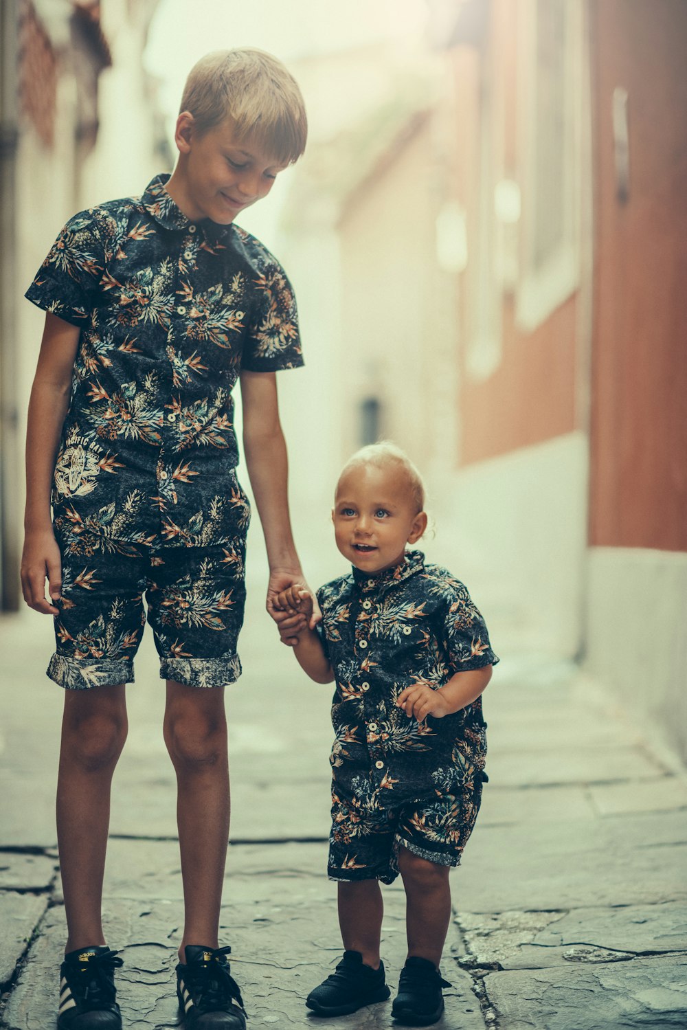 Un par a juego de camisa con cuello floral negro y gris para niño y pantalones cortos de pie sobre un área de concreto gris