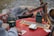 A cozy scene by a campfire, with a red table featuring two green mugs, a deck of cards, and a cribbage board. One person is holding playing cards, engrossed in a card game.