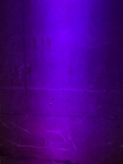 A textured concrete wall is illuminated with a soft purple light, revealing subtle grooves and imperfections on its surface.