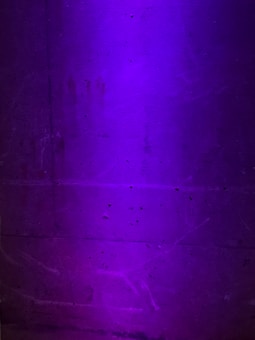 A textured concrete wall is illuminated with a soft purple light, revealing subtle grooves and imperfections on its surface.