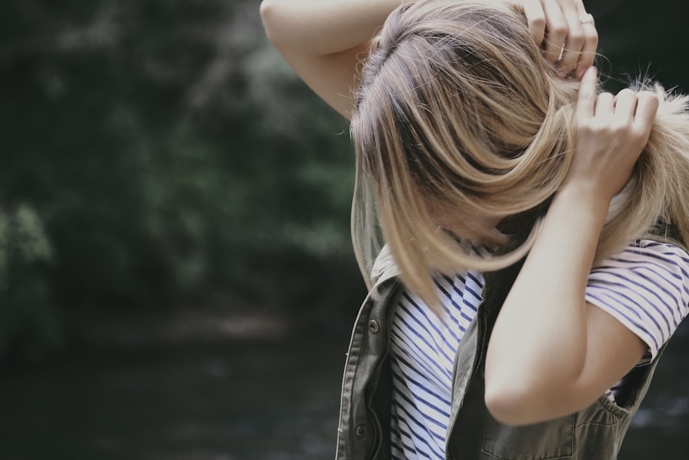 photography of a woman in striped shirt fixing her hair