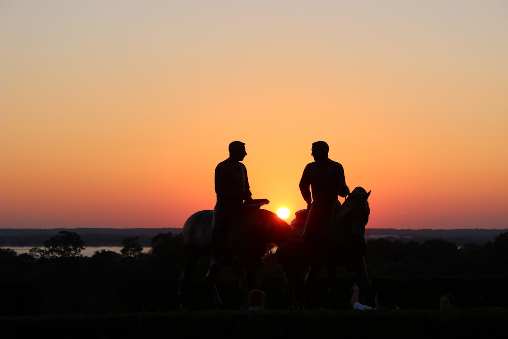Silhouette von zwei Personen, die während der goldenen Stunde auf einem Pferd reiten