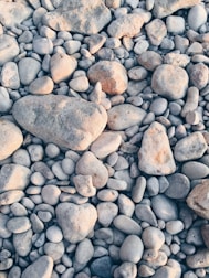 A collection of variously sized smooth stones and pebbles, ranging in color from light gray to tan, tightly packed together to form a natural, textured surface.