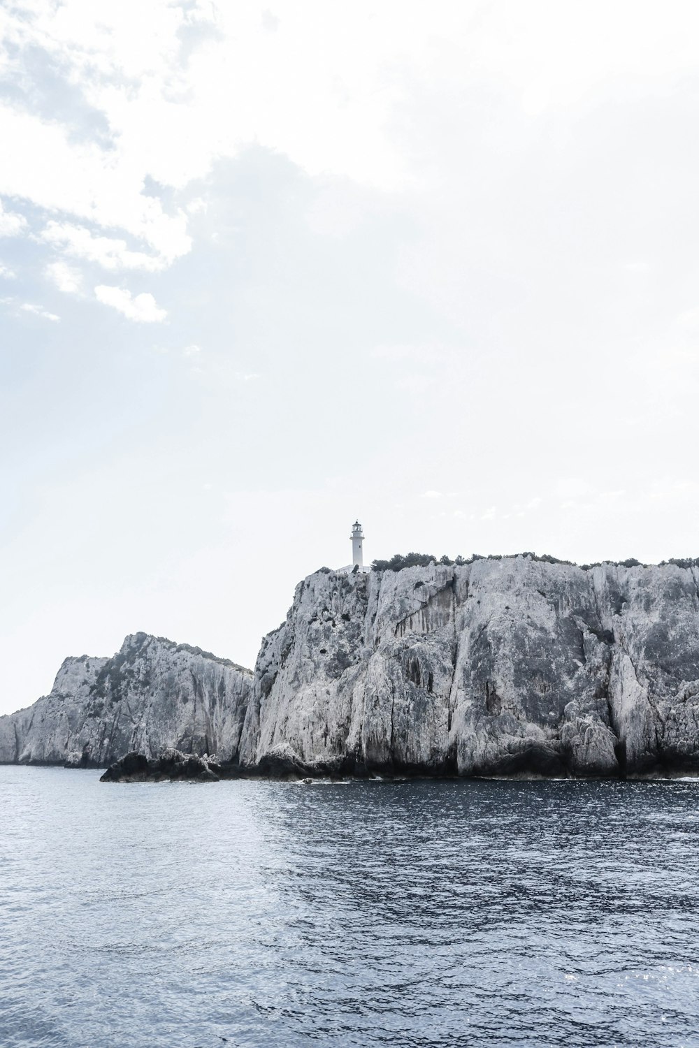 fotografia em tons de cinza do farol no penhasco