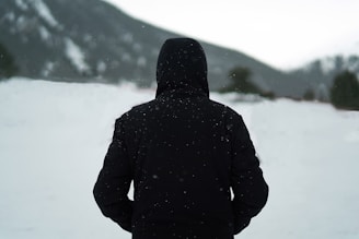 person wearing black hoodie standing on snow field during daytime