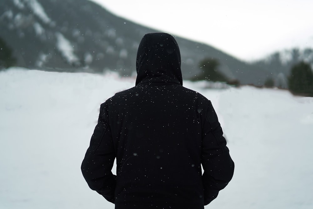 Persona che indossa una felpa con cappuccio nera in piedi sul campo di neve durante il giorno