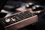 An electronic device with a wooden frame, featuring a control panel with buttons and a white knob. The device displays a red digital reading and is positioned on a dark, blurred background.