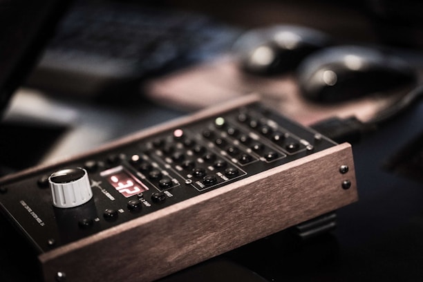An electronic device with a wooden frame, featuring a control panel with buttons and a white knob. The device displays a red digital reading and is positioned on a dark, blurred background.