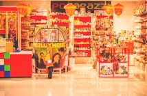 A colorful shop interior filled with a variety of items, including numerous shelves filled with decorative products. At the center is a vibrant auto-rickshaw adorned with Bollywood-themed artwork. The shop is adorned with hanging lamps and there's an array of products on display including trinkets, textiles, and ornaments.