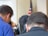 Several individuals are seated facing away from the camera, with an American flag visible in the background.