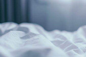 Soft waves of a white bed sheet are illuminated by a gentle light, creating a calm and serene atmosphere.