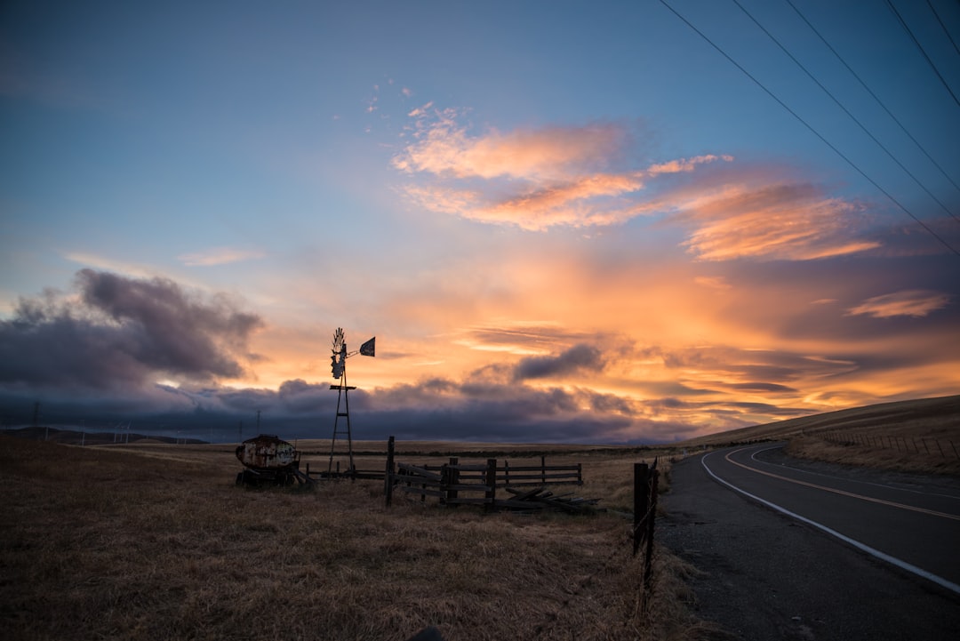 black wind mill on green field under blue and orange skies