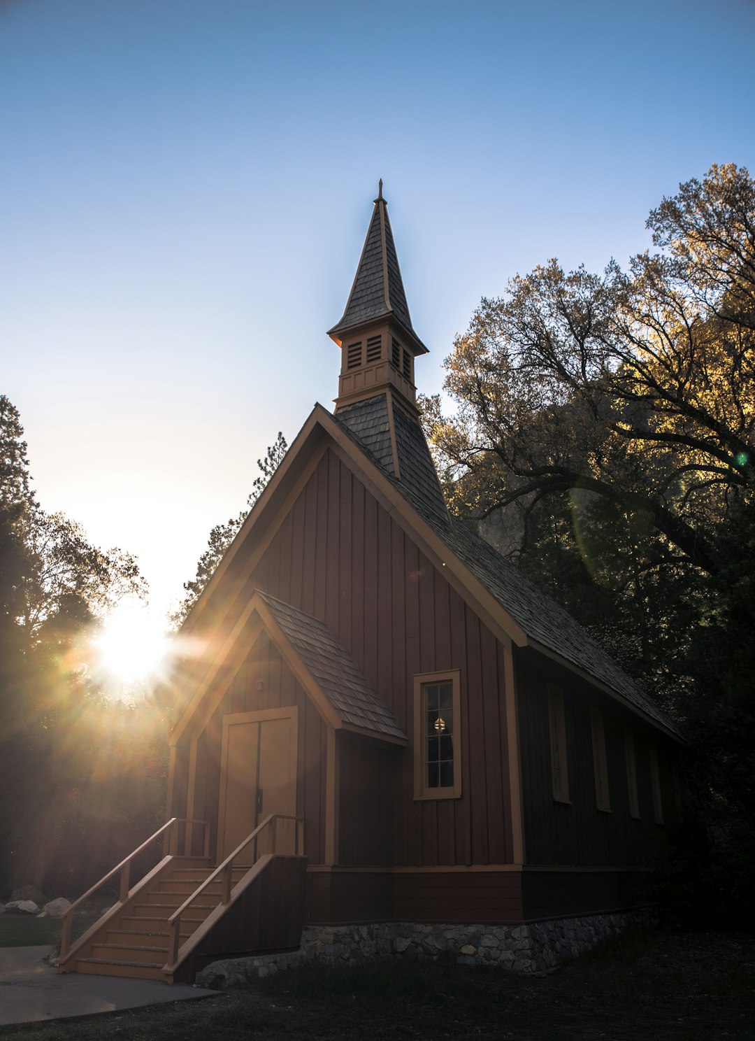 A small church building surrounded by trees, with the sunset in the background.
