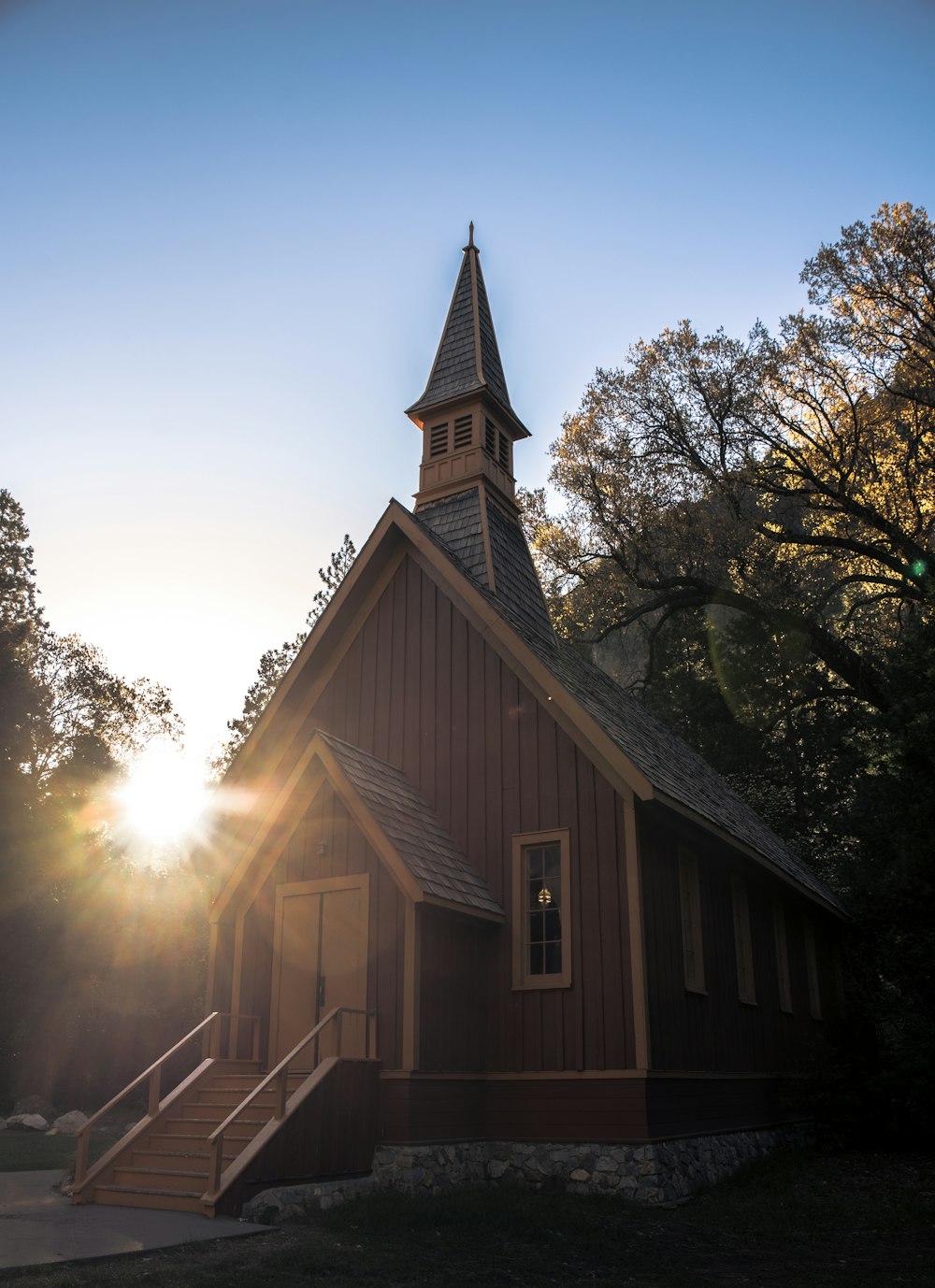 Une petite église entourée d’arbres, avec le coucher de soleil en arrière-plan.