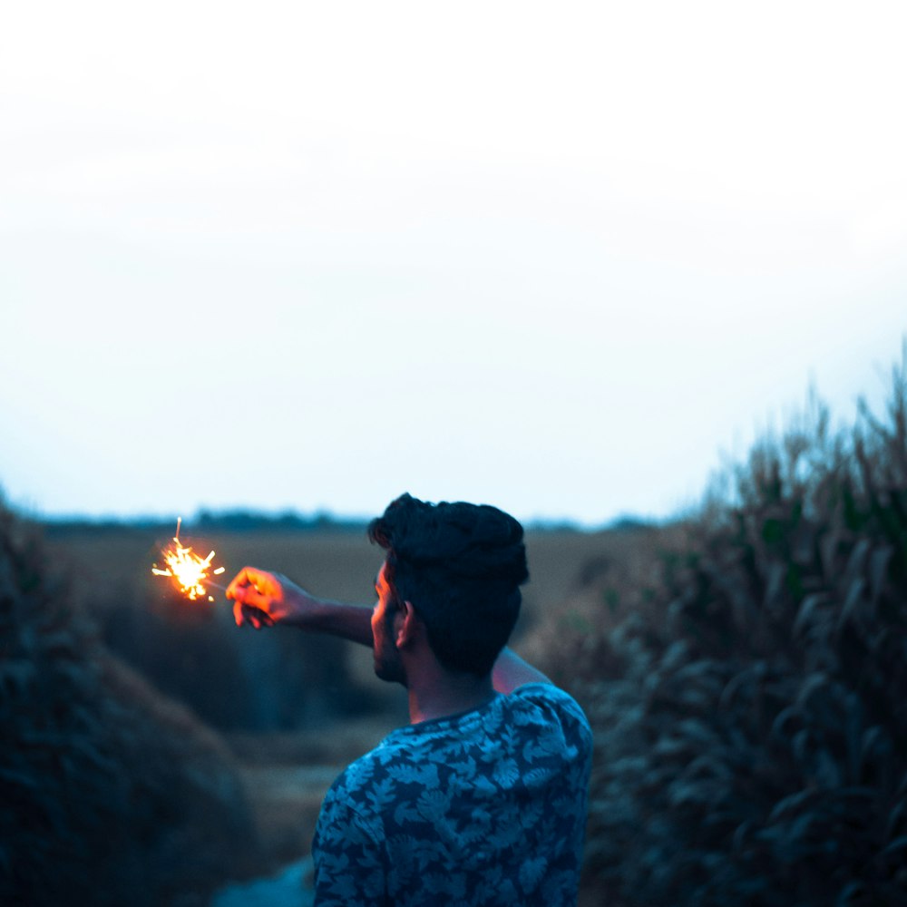 man wearing white and black floral shirt holding sparklers while standing