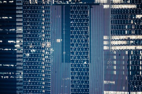 A high-rise building facade with intricate patterns illuminated against a dark background. The architecture features geometric designs with hexagonal and linear elements, reflecting a modern aesthetic. The lighting highlights sections of the structure, creating a shimmering effect.