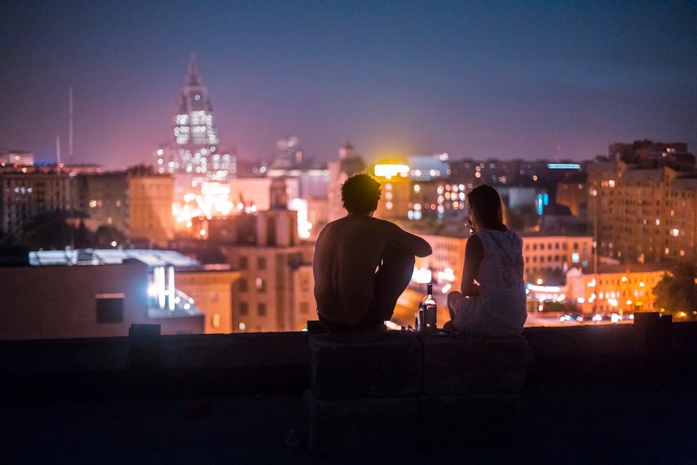 man and woman chilling on rooftop in front of high-rise buildings