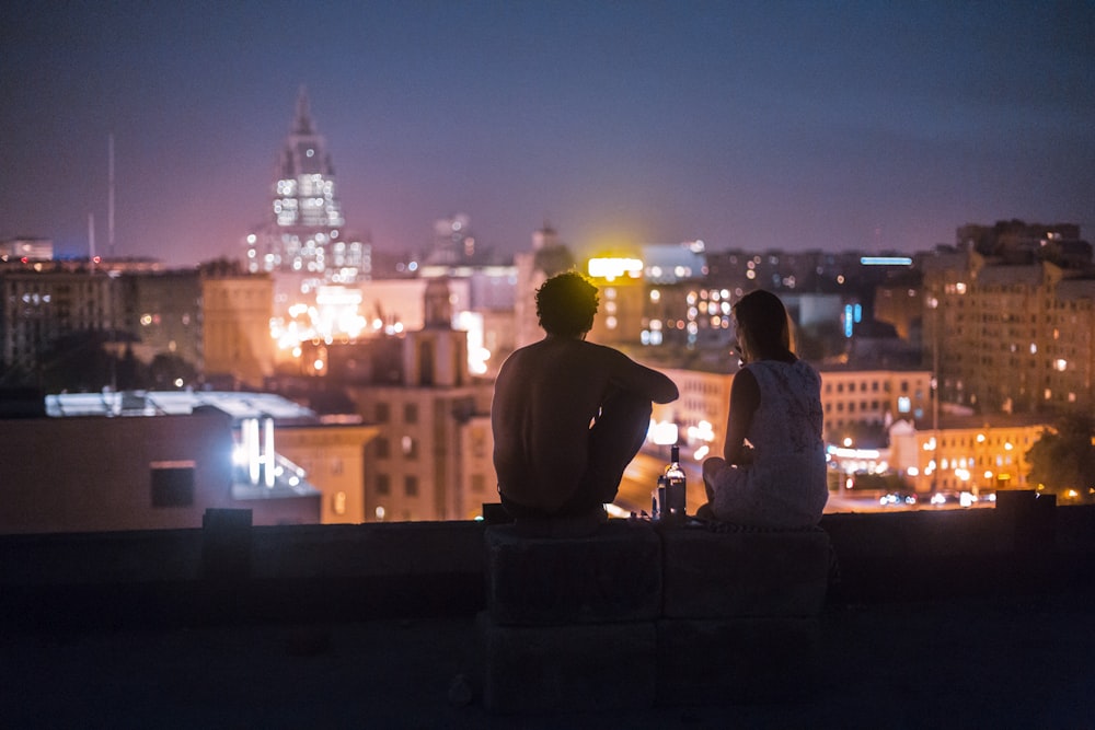 man and woman chilling on rooftop in front of high-rise buildings