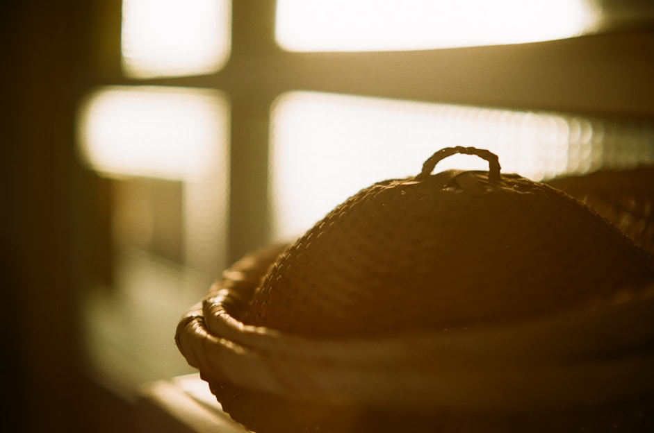 Close-up of a handcrafted bamboo basket glowing softly in warm natural light, set against a backdrop of woven textures and gentle falling bamboo leaves.
